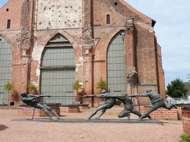 Statue of people engaged in a tug of war in front of a building